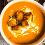 A bowl of roasted sweet potato soup swirled with cream, topped with croutons and thyme sprigs.