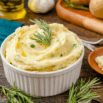 Bowl of rosemary garlic mashed potatoes garnished with fresh rosemary sprigs and herbs.