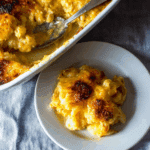 Southern baked macaroni and cheese with a golden, crispy cheese topping, served on a white plate beside a baking dish.