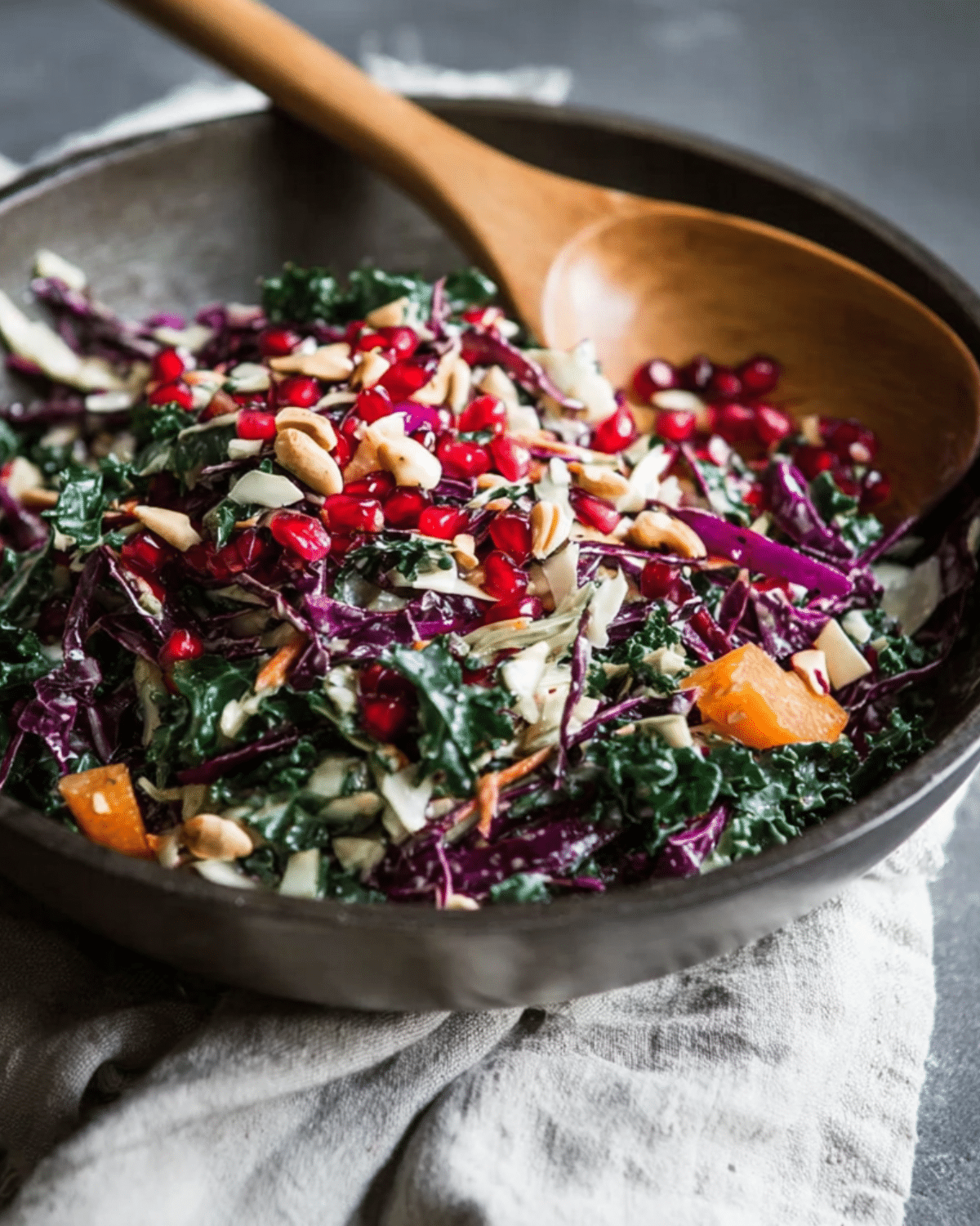 Bowl of colorful winter veggie coleslaw with kale, red cabbage, pomegranate seeds, nuts, and seasonal vegetables.