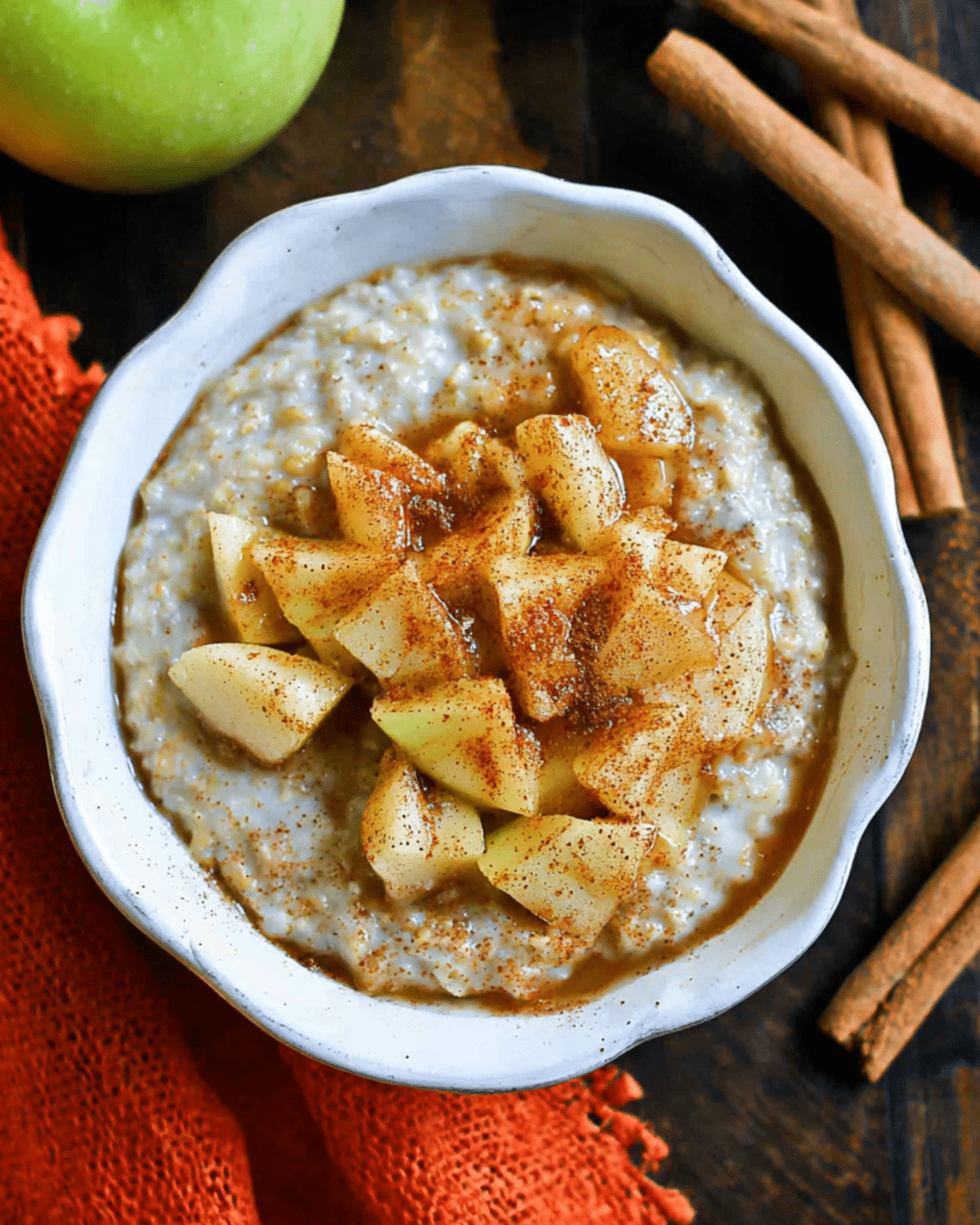 Bowl of apple and cinnamon porridge topped with spiced apple chunks and a sprinkle of ground cinnamon.