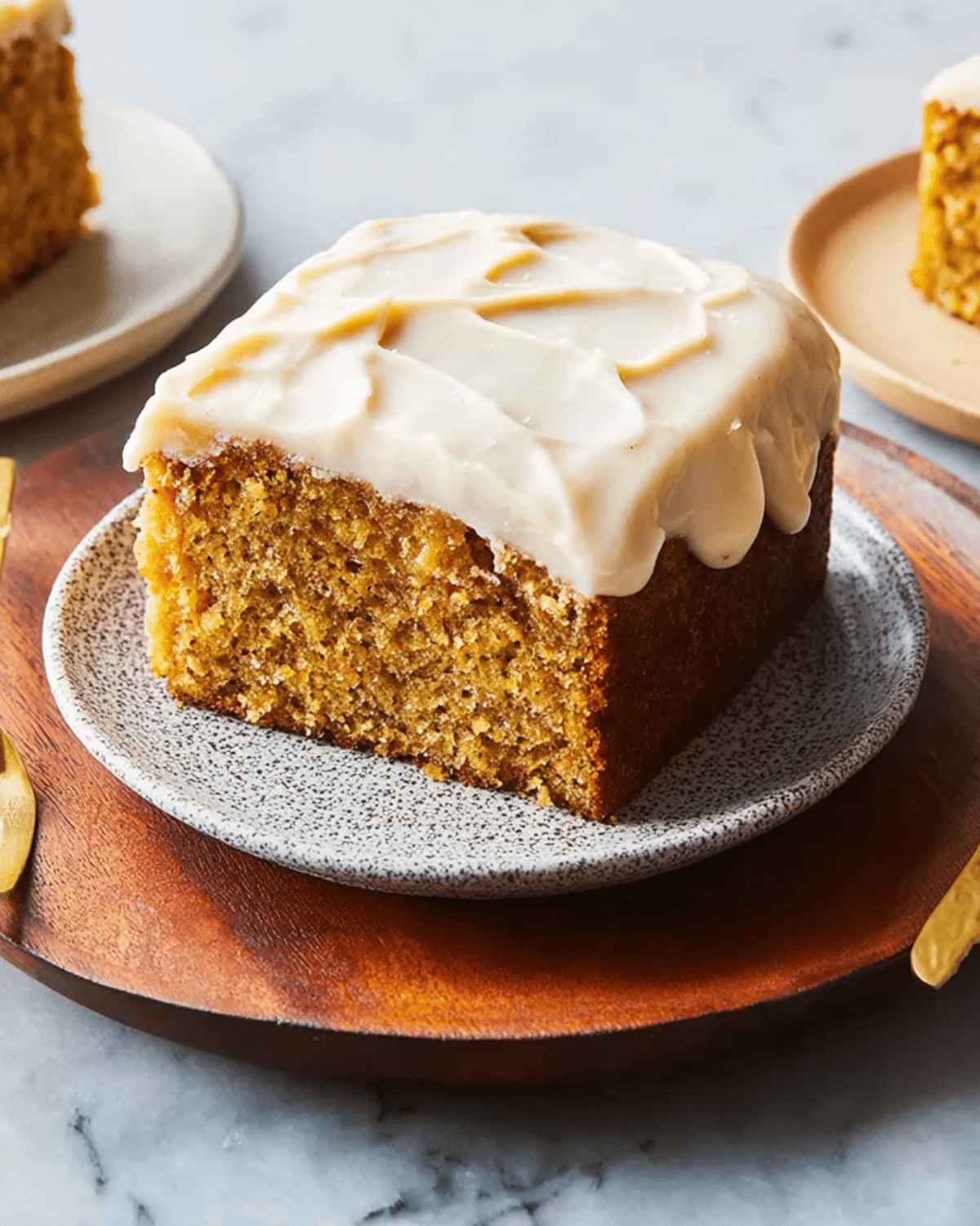 Square slice of moist Applesauce Cake topped with creamy frosting, served on a ceramic plate with a wooden charger.