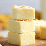 Stacked cubes of creamy banana fudge on a wooden board, with a soft yellow hue and smooth texture.