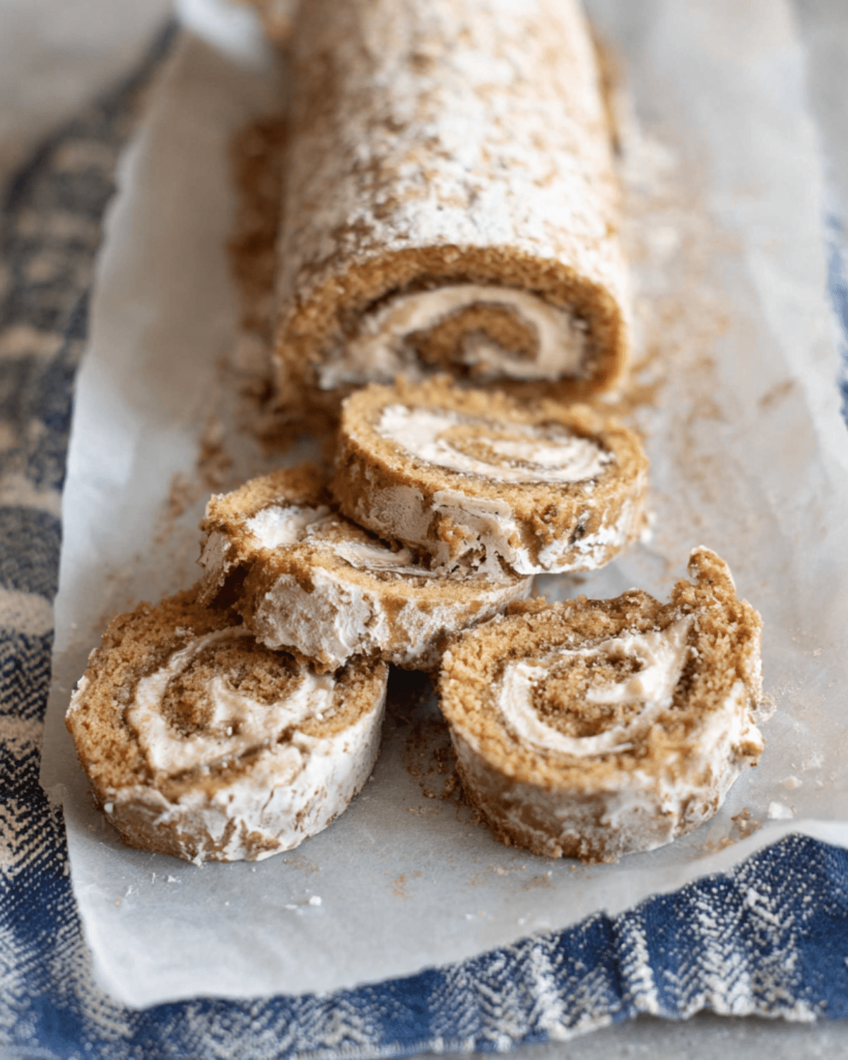Sliced banana roll cake filled with cream and dusted with powdered sugar on parchment paper.