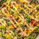 A bowl of Big Mac salad made with ground beef, shredded lettuce, cherry tomatoes, cheddar cheese, red onions, and drizzled with special sauce.