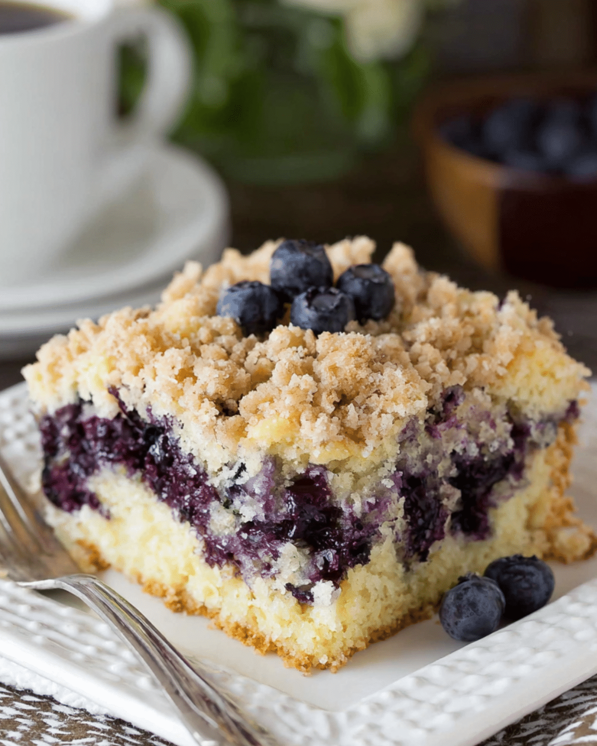 A slice of Blueberry Breakfast Cake with a crumb topping, filled with fresh blueberries and served on a white plate.