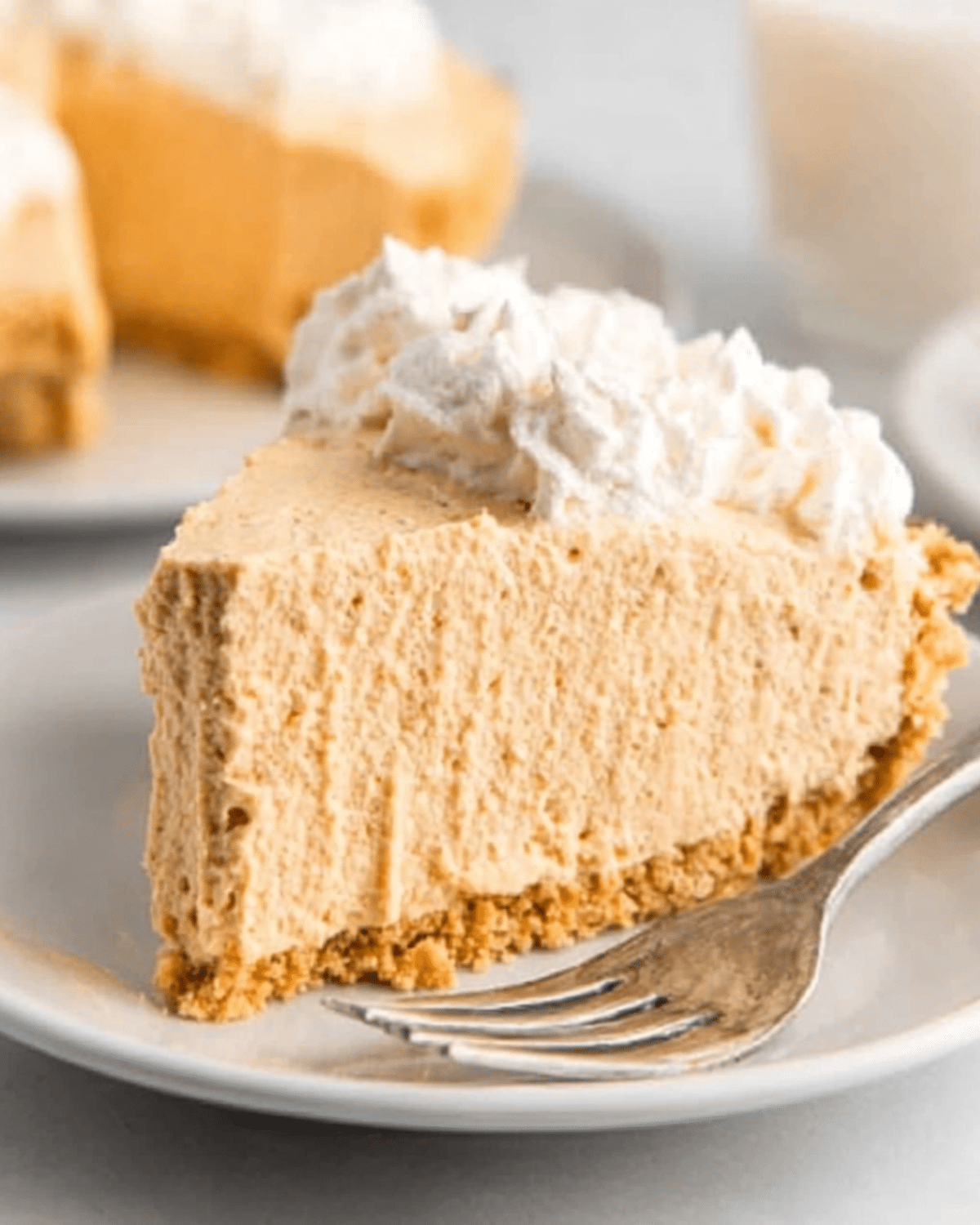A slice of butterscotch Cool Whip pie topped with whipped cream on a white plate with a fork.