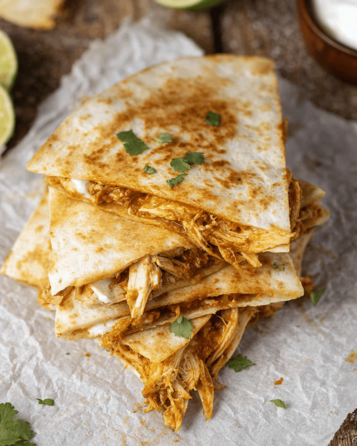 Stacked Crockpot Queso Chicken Quesadillas filled with shredded cheesy chicken on a parchment-lined surface.