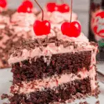 Slice of Cherry Dr Pepper Cake with chocolate cake layers, pink cherry frosting, chocolate shavings, and a maraschino cherry on top.