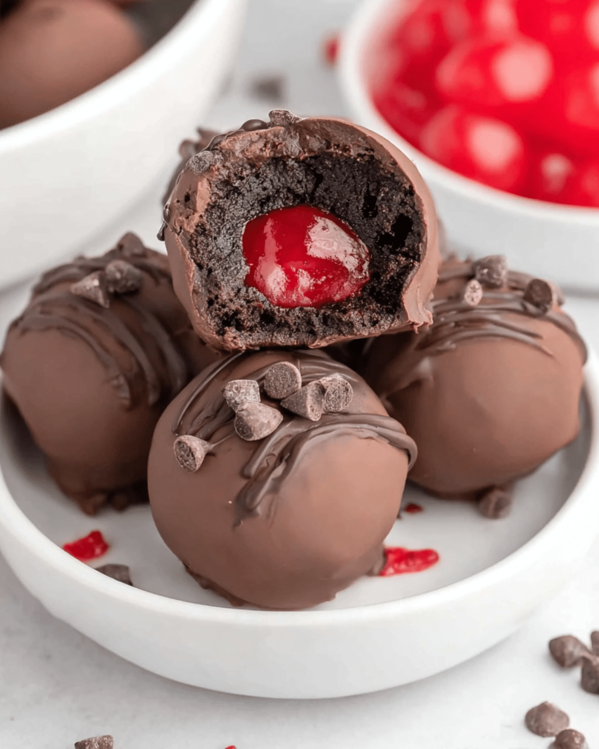 Bowl of chocolate covered cherry brownie bombs topped with mini chocolate chips, with one cut open to reveal a cherry center inside a rich brownie filling.