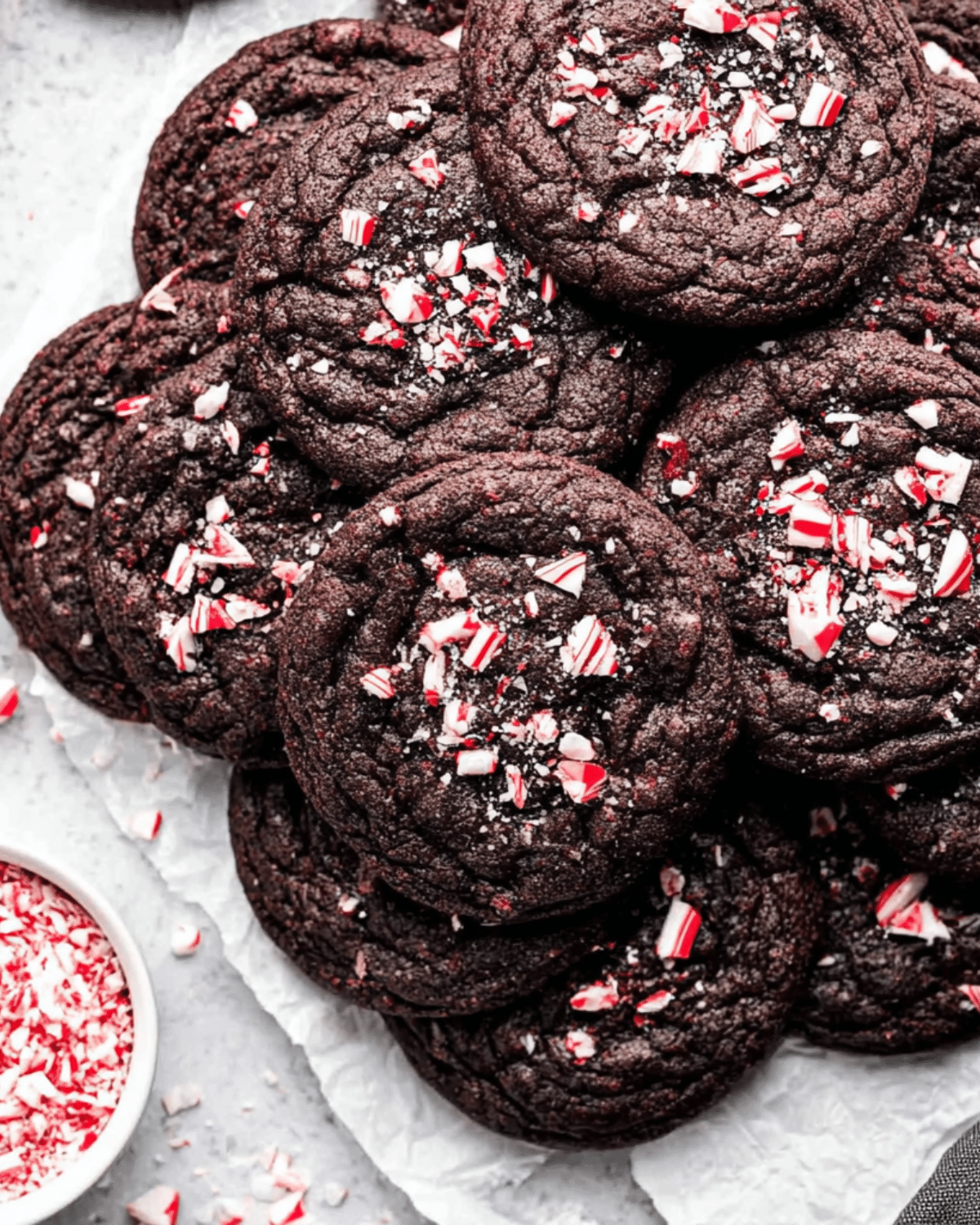 A stack of chocolate peppermint cookies topped with crushed candy canes on parchment paper.