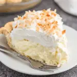 Slice of coconut cream pie with a flaky crust, creamy coconut filling, fluffy whipped topping, and toasted coconut flakes on top.