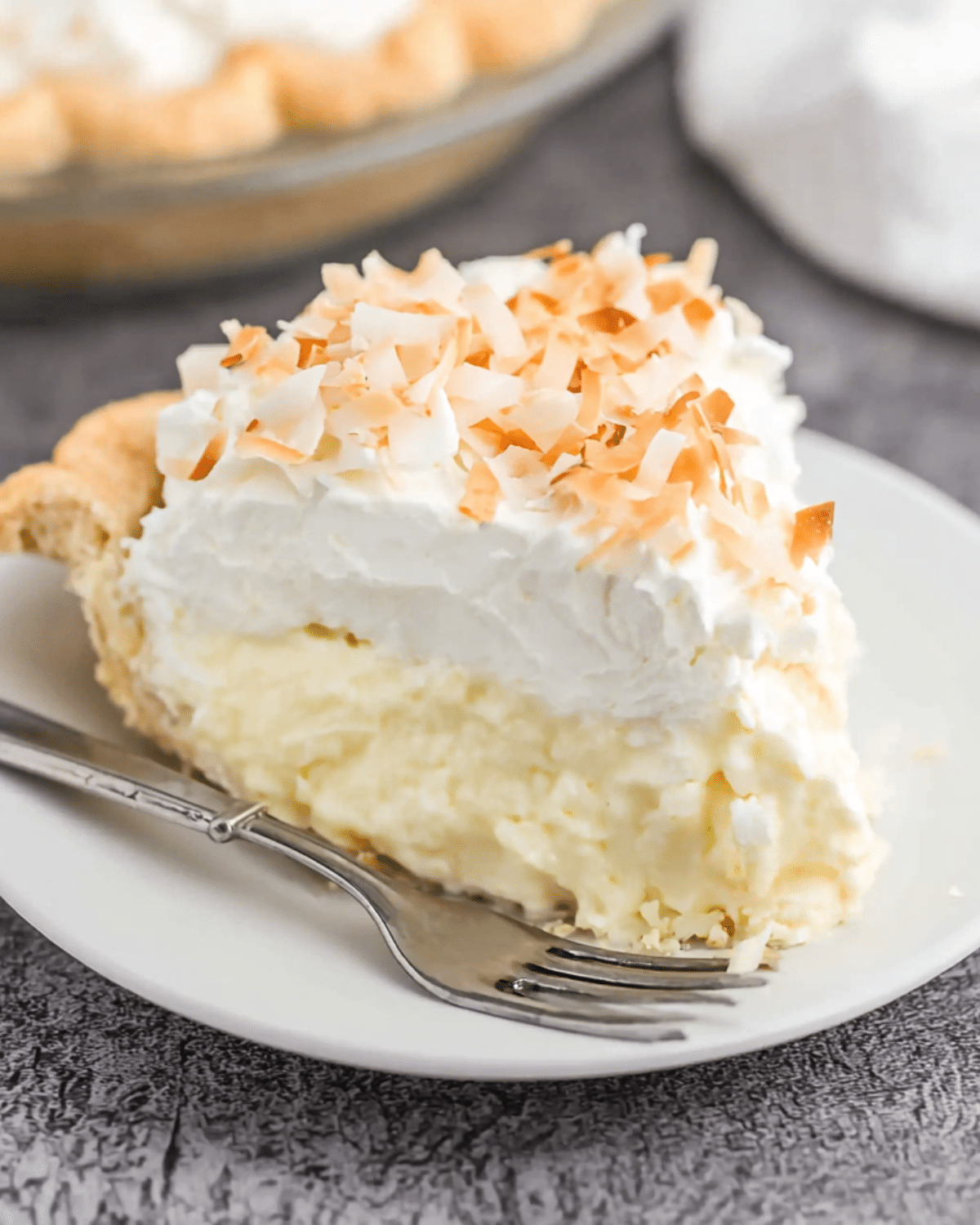 Slice of coconut cream pie with a flaky crust, creamy coconut filling, fluffy whipped topping, and toasted coconut flakes on top.