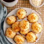 Golden-baked coconut macaroons arranged on a white plate, with shredded coconut scattered around.