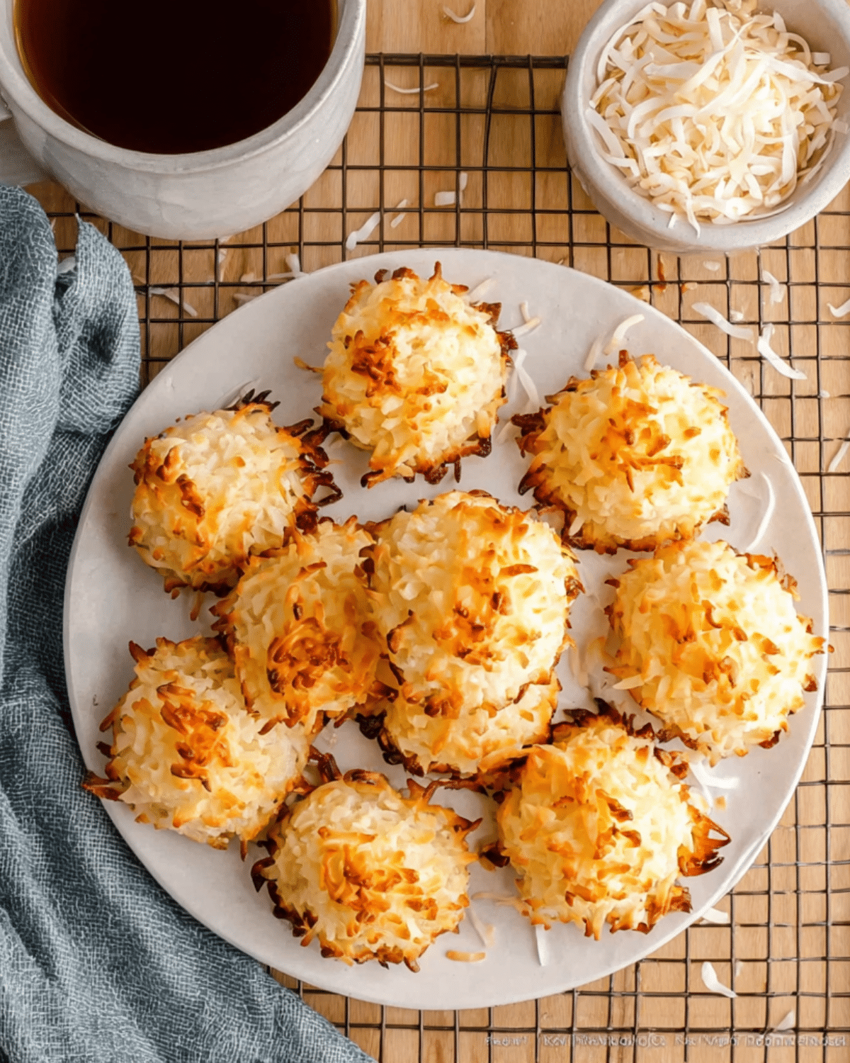 Golden-baked coconut macaroons arranged on a white plate, with shredded coconut scattered around.