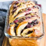 Freshly baked cranberry pistachio babka in a glass loaf pan, swirled with cranberry filling and sprinkled with chopped pistachios.
