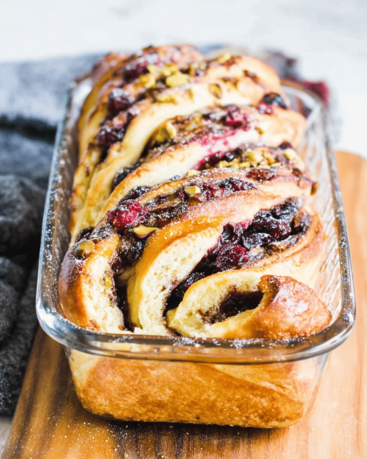Freshly baked cranberry pistachio babka in a glass loaf pan, swirled with cranberry filling and sprinkled with chopped pistachios.