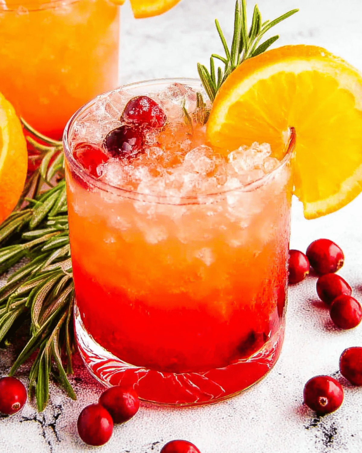 Glass of cranberry orange Christmas punch garnished with cranberries, orange slice, and rosemary sprig, surrounded by fresh cranberries.