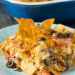 Serving of Doritos cheesy chicken casserole on a plate, filled with shredded chicken, melted cheese, olives, tomatoes, and crunchy Doritos chips.