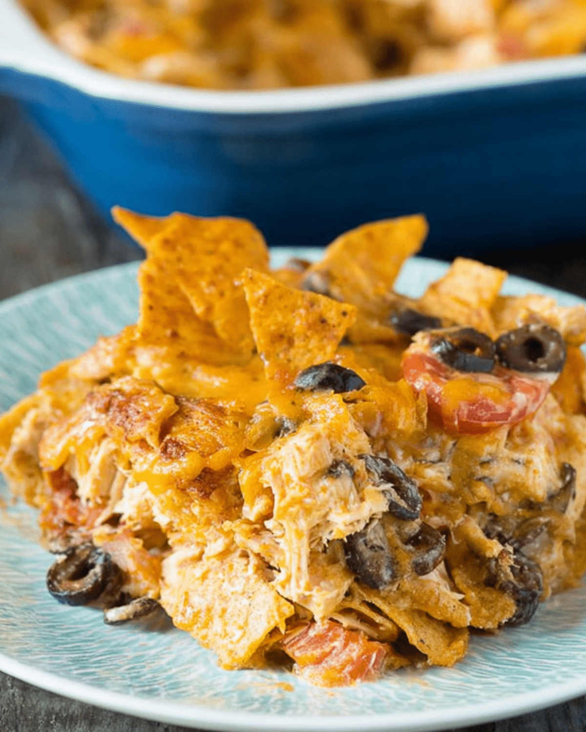 Serving of Doritos cheesy chicken casserole on a plate, filled with shredded chicken, melted cheese, olives, tomatoes, and crunchy Doritos chips.