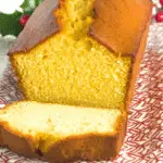 Golden-brown eggnog bread loaf with a slice cut, showing its moist and fluffy interior, served on a festive red and white patterned plate.