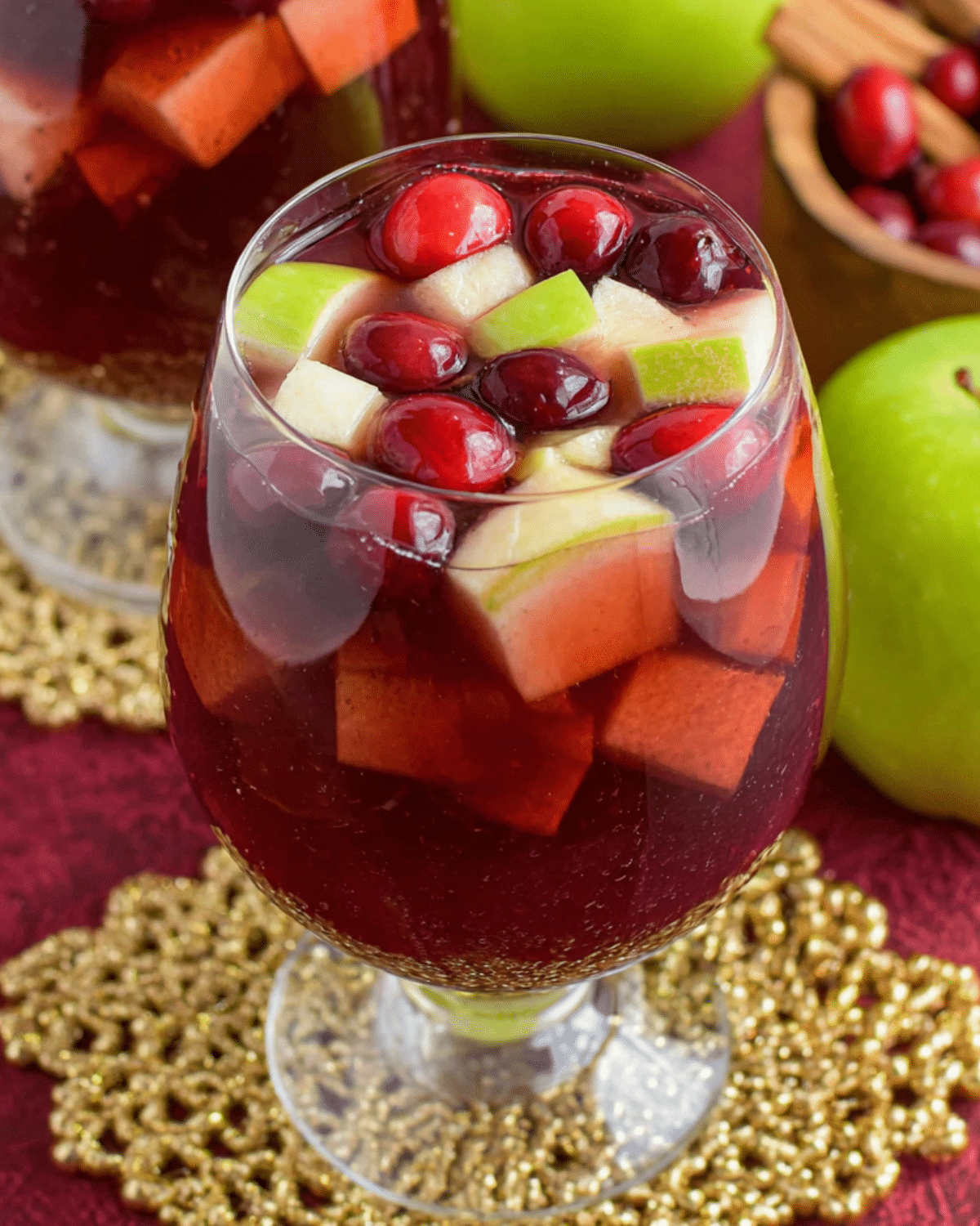 A glass of Fireball Sangria filled with red liquid, floating cranberries, and diced green and red apples.
