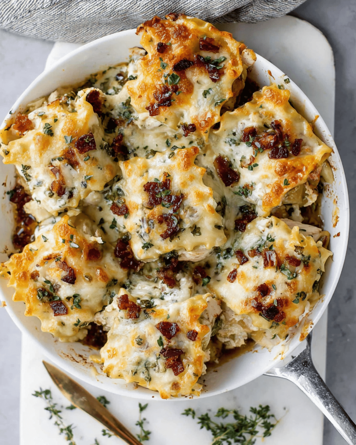 Baking dish filled with cheesy French onion chicken lasagna roll ups, topped with herbs and caramelized onions.