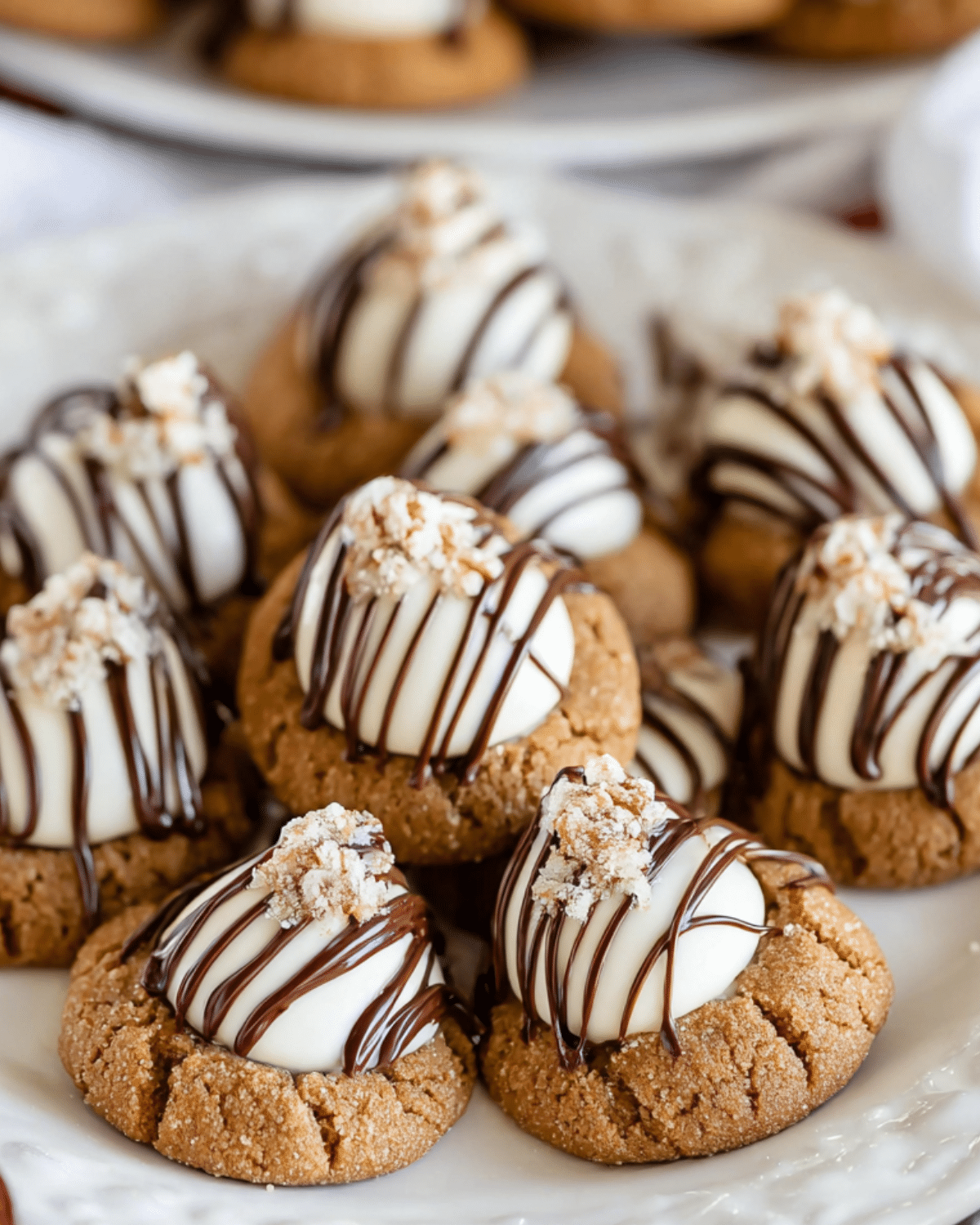 Plate of Gingerbread Kiss Cookies topped with white chocolate kisses, drizzled with dark chocolate, and sprinkled with crushed candied ginger.