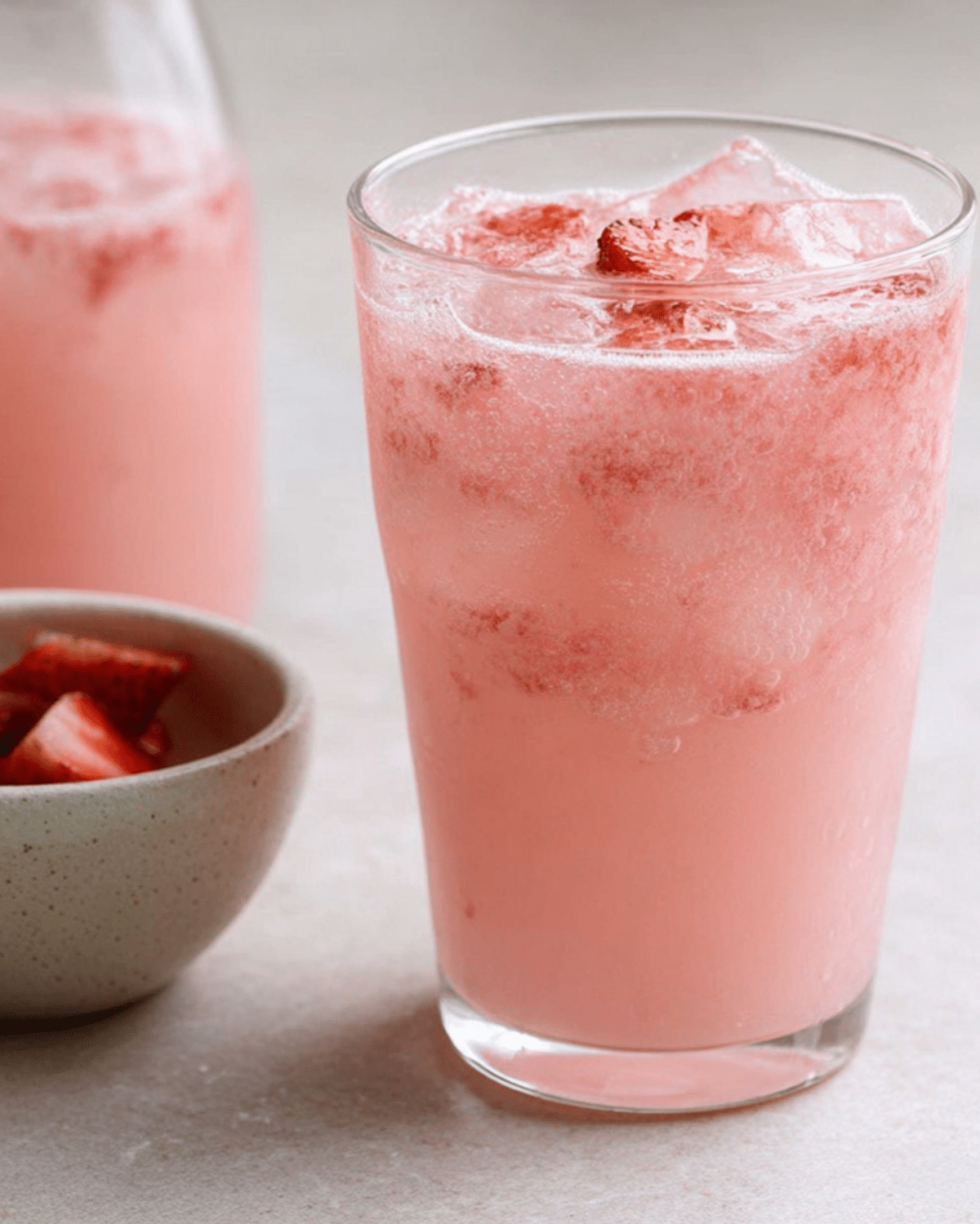 A glass of refreshing Homemade Pink Drink with ice and fresh strawberry pieces.
