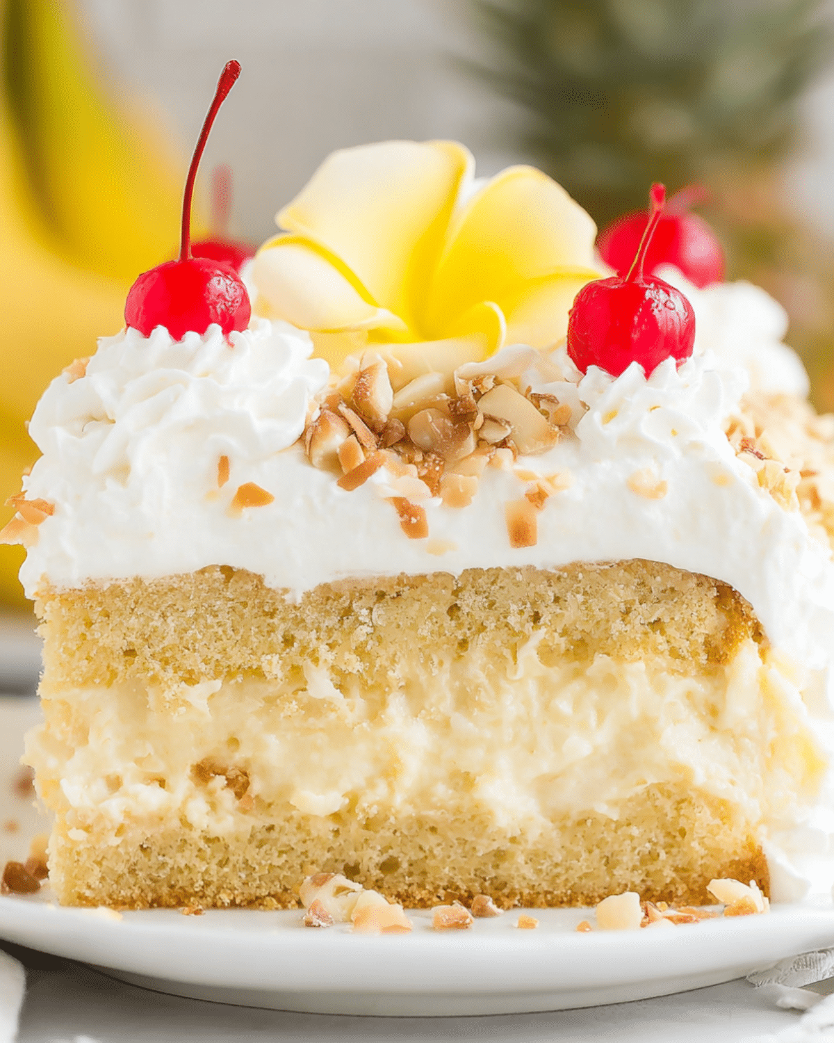 Slice of Hawaiian Wedding Cake with fluffy yellow cake layers, creamy pineapple filling, whipped topping, cherries, toasted coconut, and macadamia nuts.