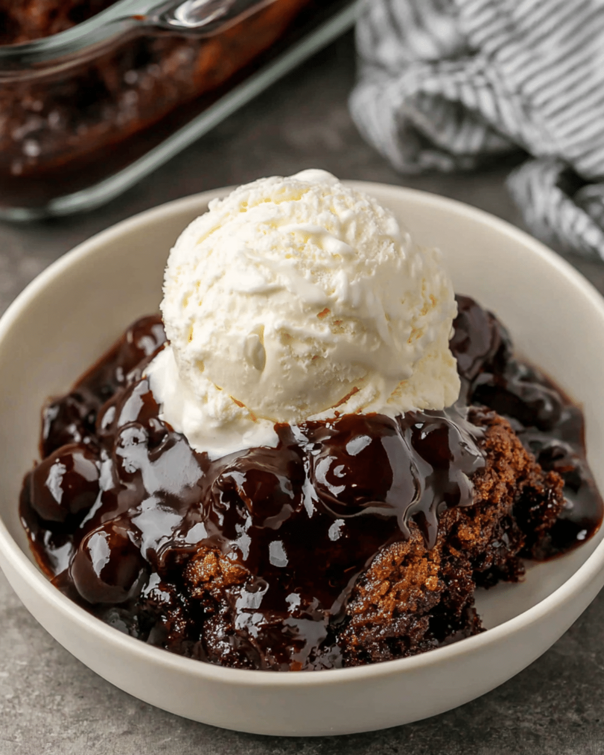 A bowl of hot fudge sundae cake topped with a scoop of vanilla ice cream and rich, glossy hot fudge sauce.