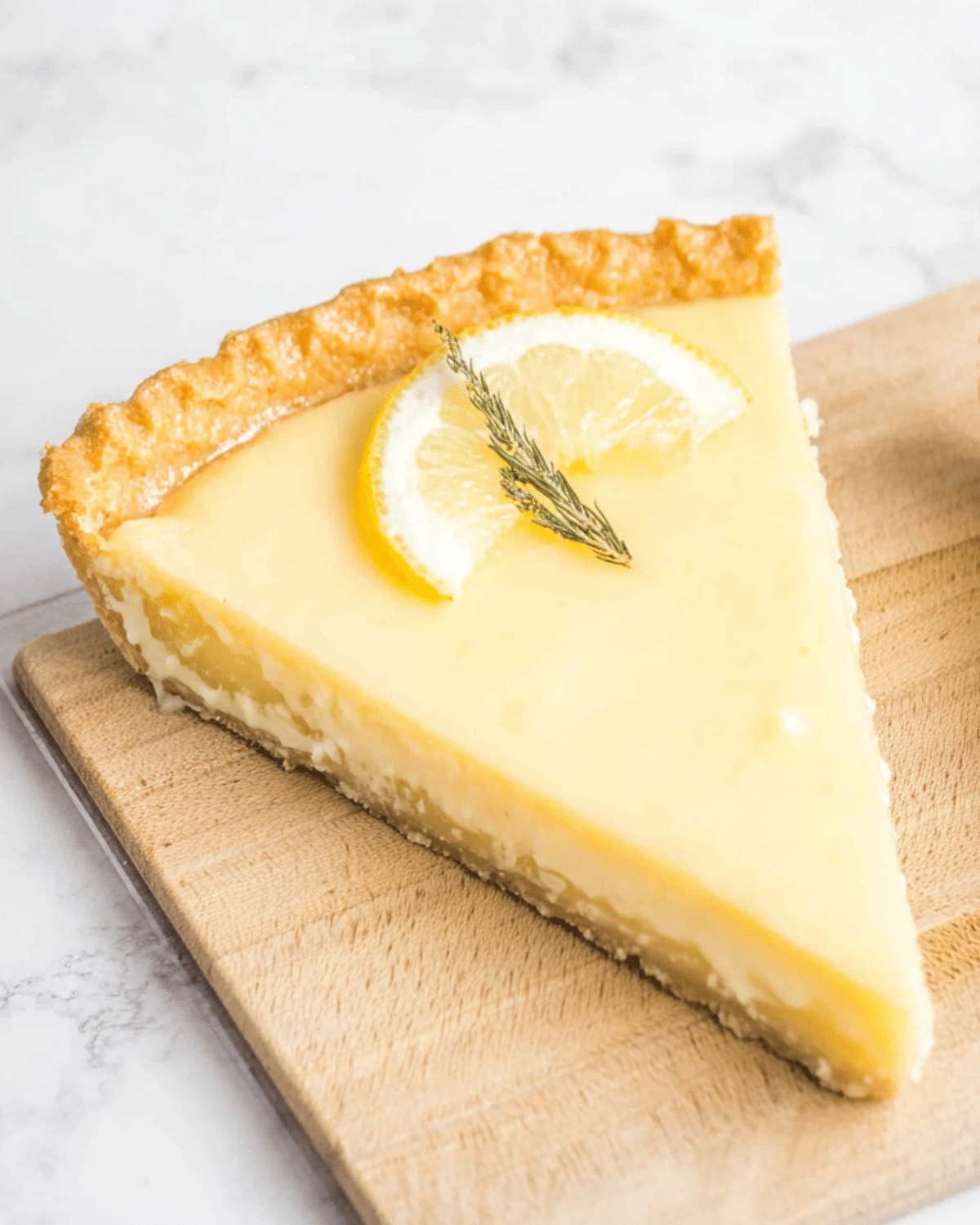 Slice of Meyer lemon pie with a golden crust, creamy lemon filling, and a lemon slice garnish on top.