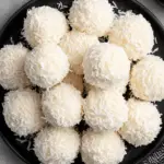 A plate of no bake coconut snowballs, coated in shredded coconut and arranged neatly on a black plate.
