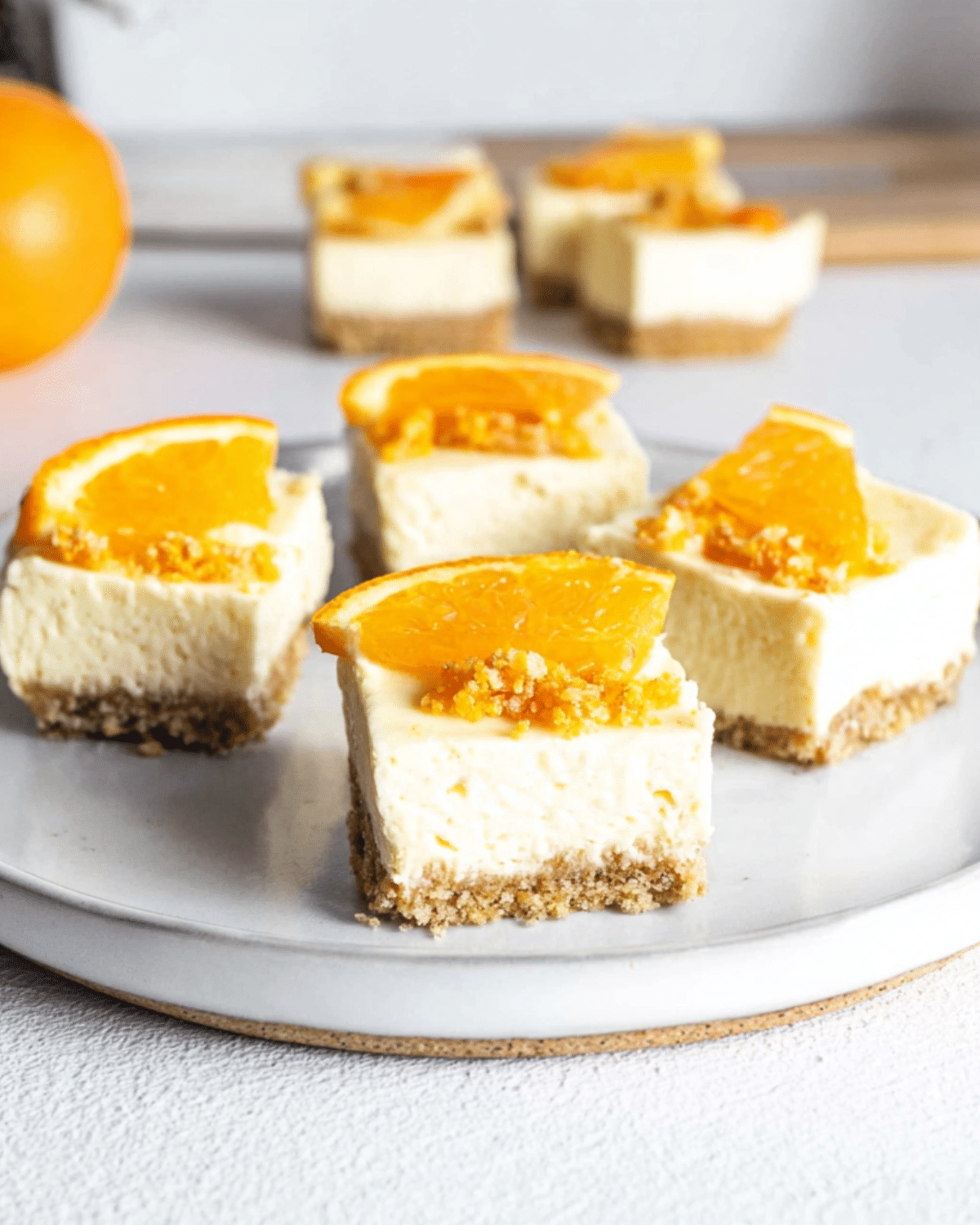 Orange Creamsicle Cheesecake Bars topped with orange slices and set on a graham cracker crust, displayed on a white plate.