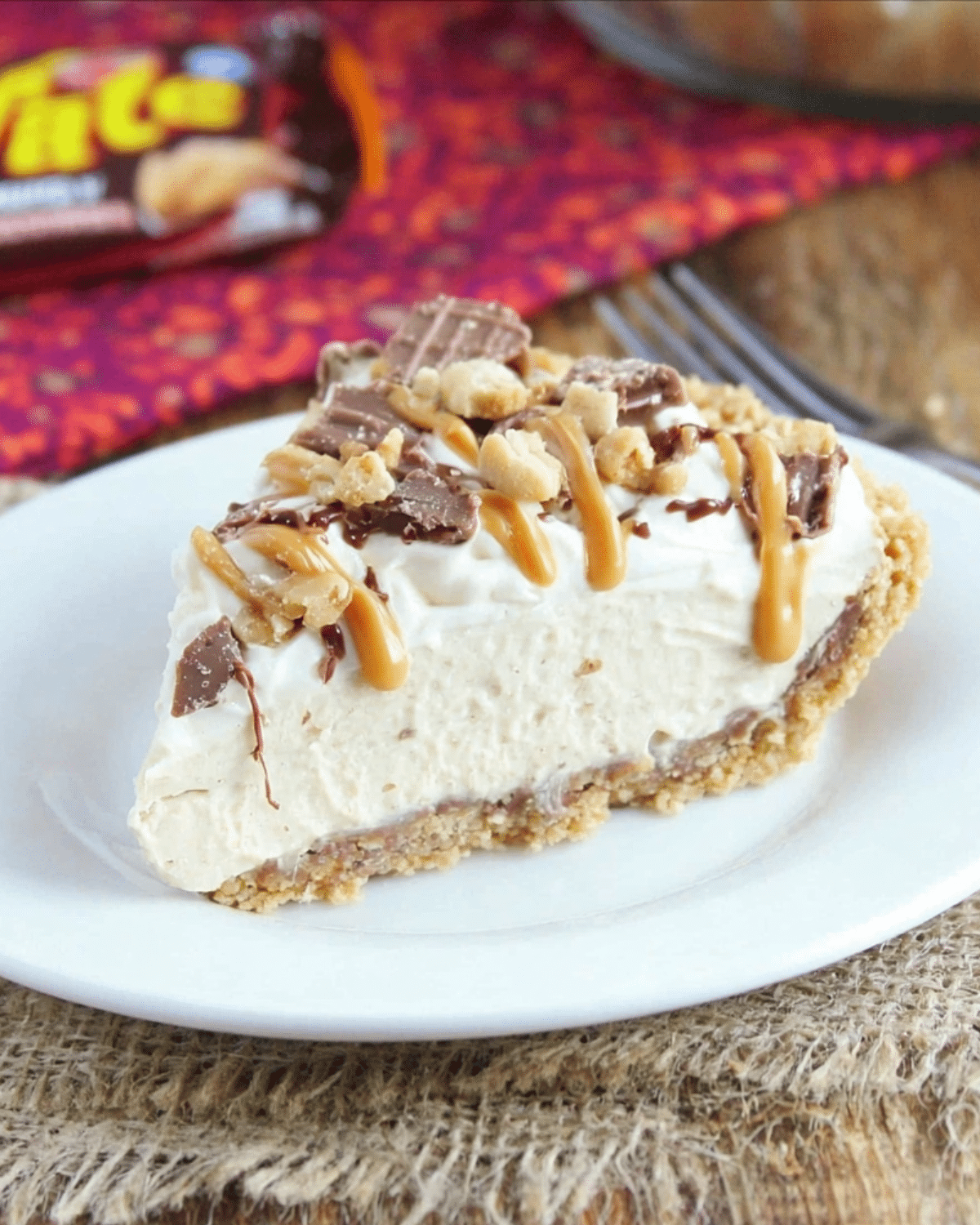 A slice of Peanut Butter Whatchamacallit Pie topped with chopped candy bars, peanuts, and caramel drizzle.