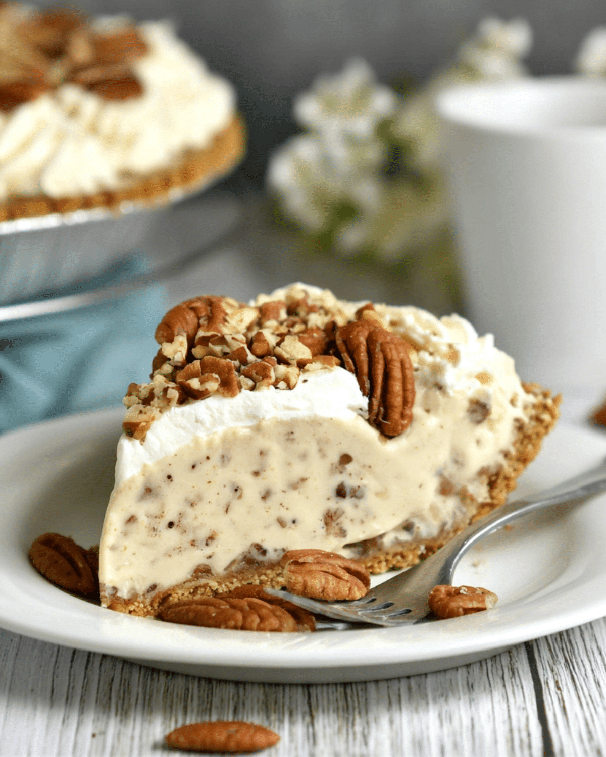 Slice of Pecan Cream Pie topped with whipped cream and chopped pecans, served on a white plate with a fork.