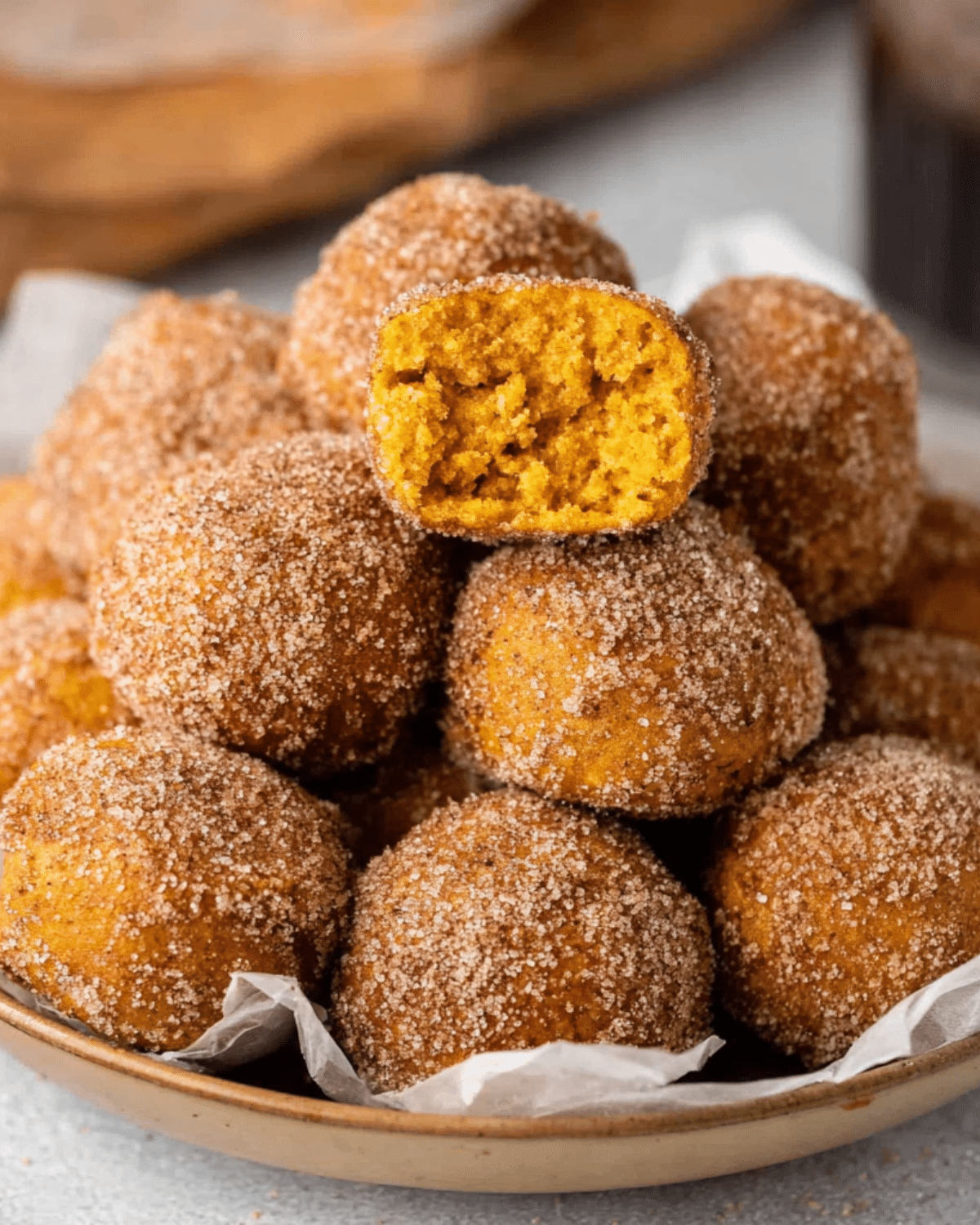 Plate of pumpkin donut holes coated in cinnamon sugar, with one cut open to show the soft, moist pumpkin interior.