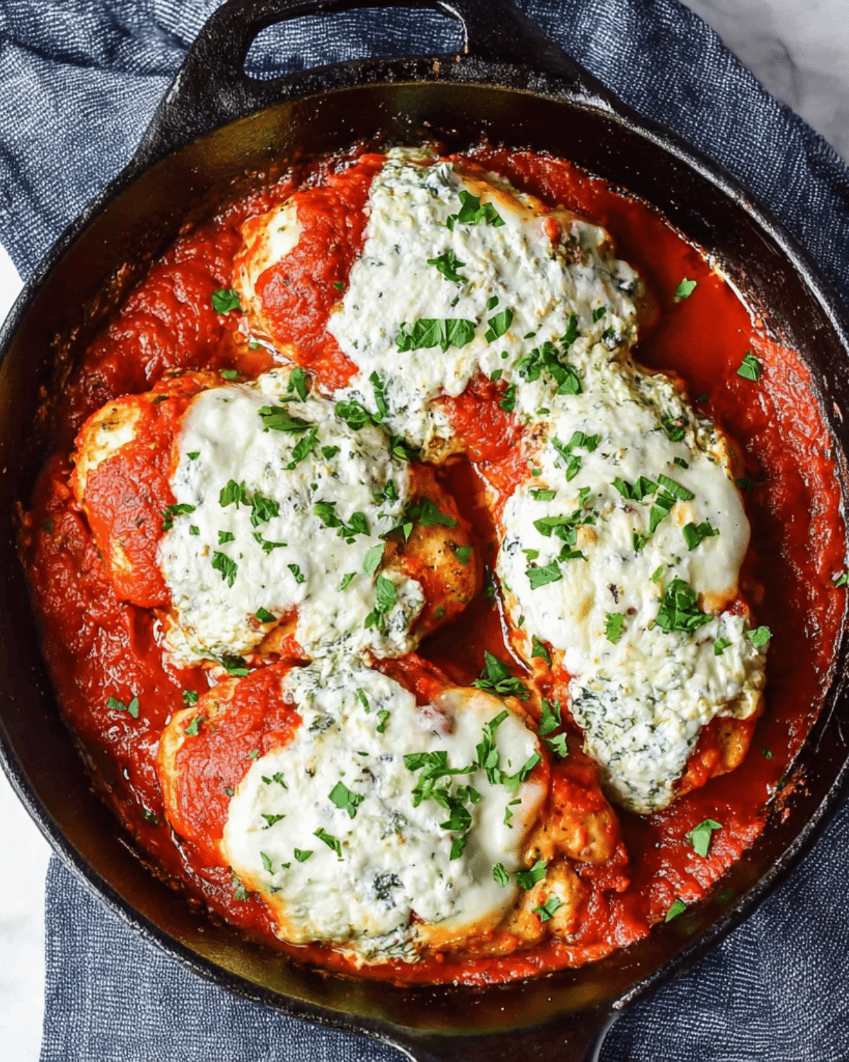 Skillet filled with Ricotta Chicken Bake, featuring chicken breasts topped with ricotta cheese and marinara sauce, garnished with fresh herbs.