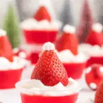 Festive Santa Hat Jello Shots topped with whipped cream and fresh strawberries, styled to resemble Santa hats.