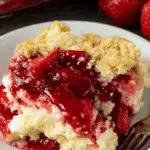 A serving of strawberry cheesecake dump cake on a white plate, showing layers of cake, creamy cheesecake, and strawberry topping.