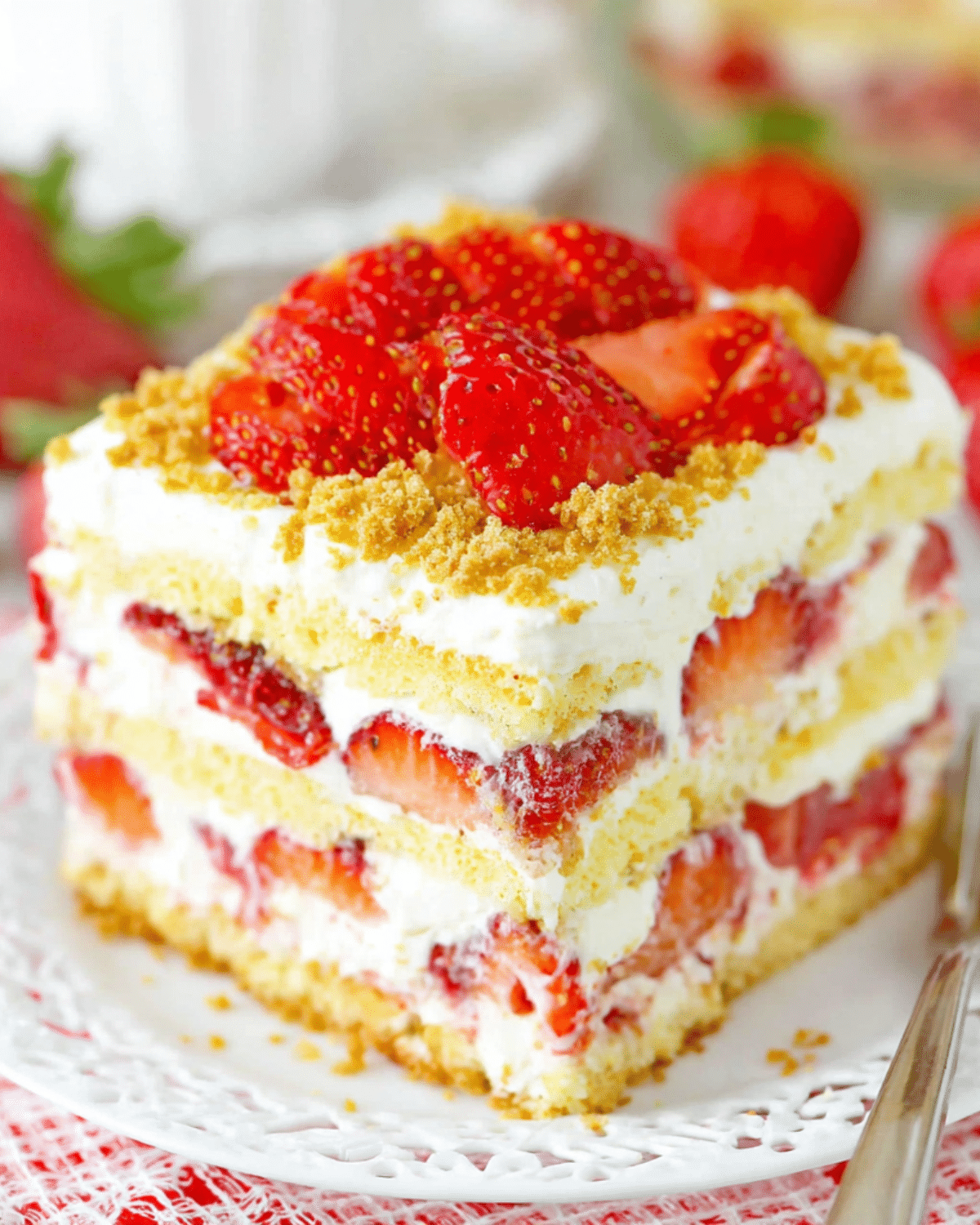 A layered slice of Strawberry Shortcake Icebox Cake with whipped cream, fresh strawberries, and crumbled cookie topping.