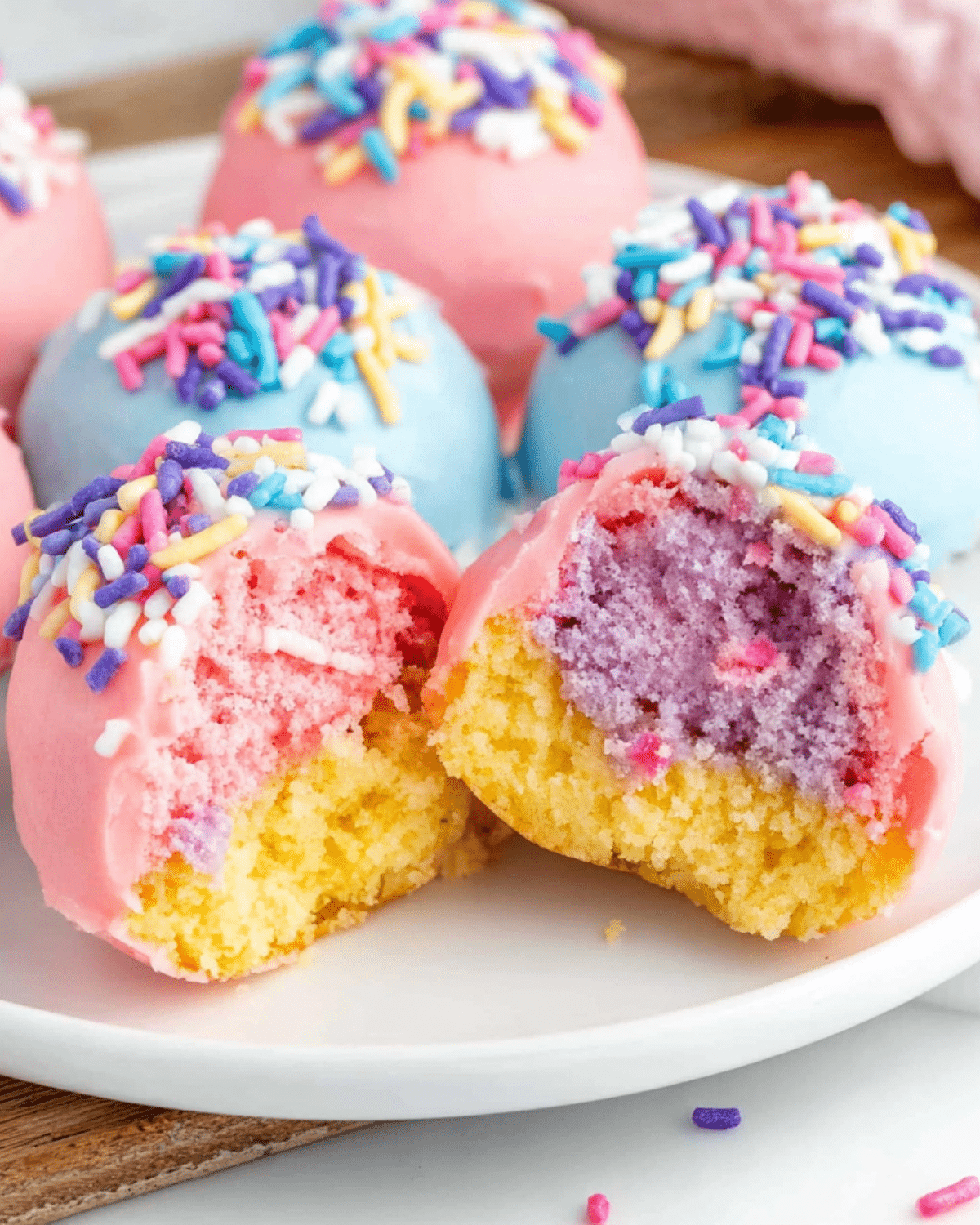 Colorful Unicorn Cheesecake Bites with pink, purple, and yellow layers, coated in pastel chocolate and topped with rainbow sprinkles.