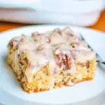 A slice of butter pecan praline poke cake topped with creamy praline glaze and crunchy pecans, served on a white plate.