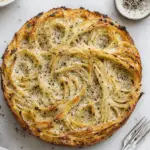 Cacio e pepe pie made with baked spaghetti, seasoned with cracked black pepper and cheese, served on a marble surface.