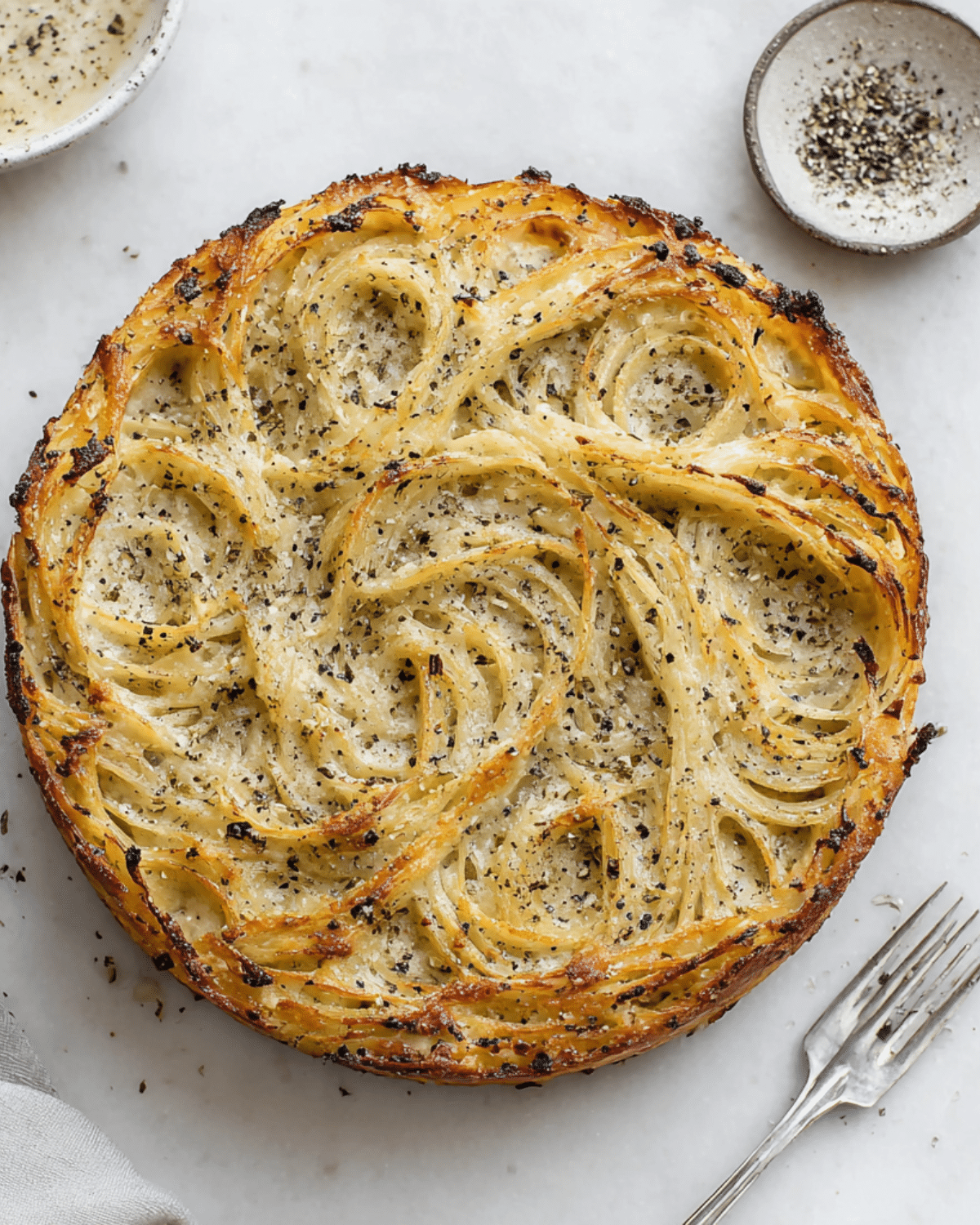 Cacio e pepe pie made with baked spaghetti, seasoned with cracked black pepper and cheese, served on a marble surface.