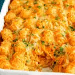 A baked dish of chicken pot pie with tater tots, topped with melted cheese and parsley.