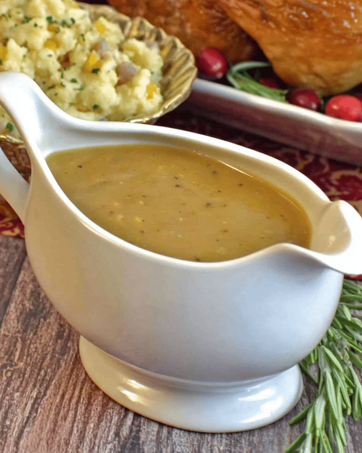 A white gravy boat filled with rich, homemade giblet gravy, surrounded by mashed potatoes, turkey, and herbs.