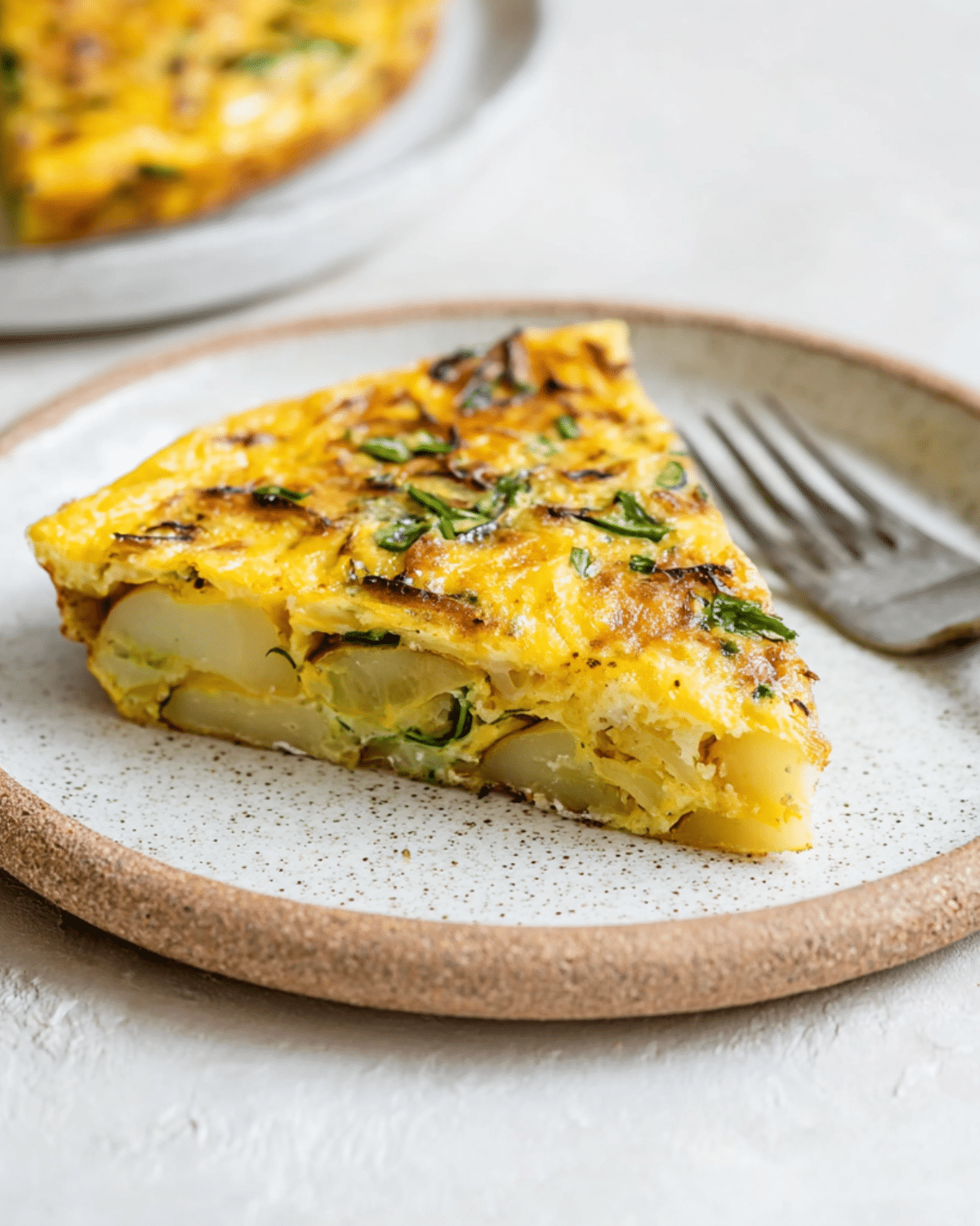 A slice of healthy potato frittata served on a ceramic plate, showing layers of potatoes, eggs, and herbs.