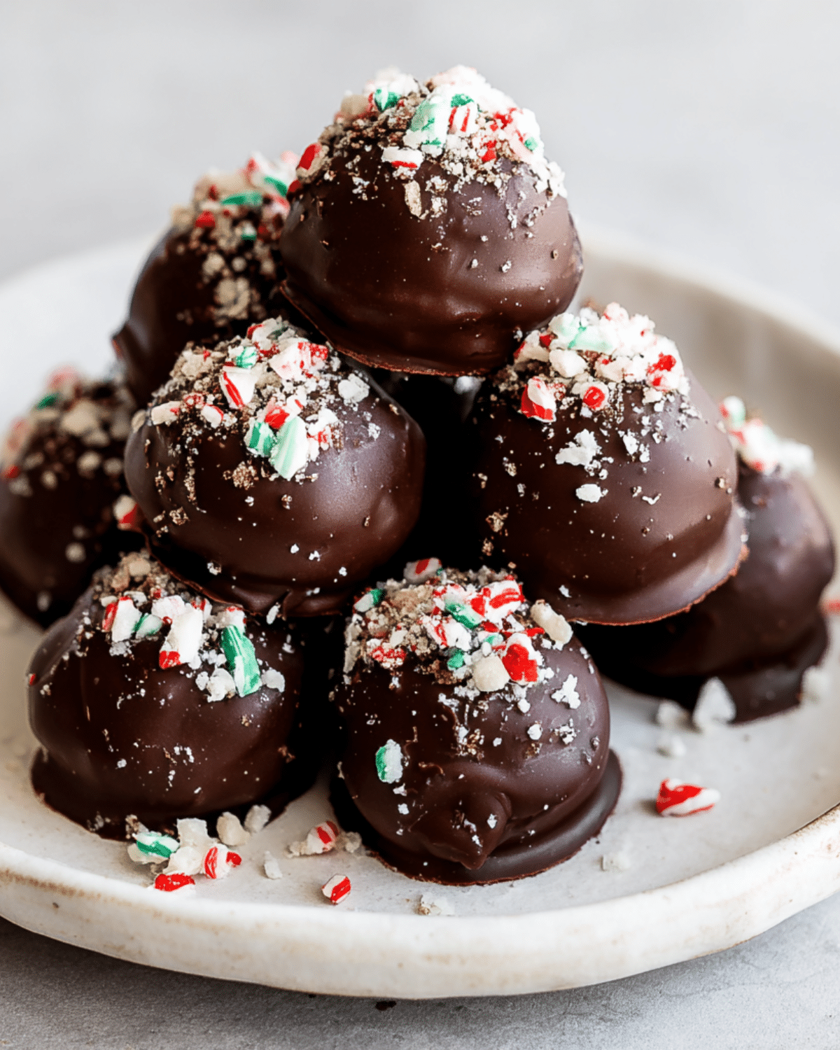 A plate stacked with peppermint Oreo truffle balls coated in dark chocolate and topped with crushed candy canes.