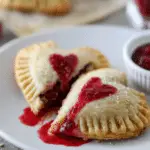 Golden raspberry Nutella heart pies on a white plate, filled with raspberry sauce and Nutella, with heart-shaped cutouts and sugar on top.